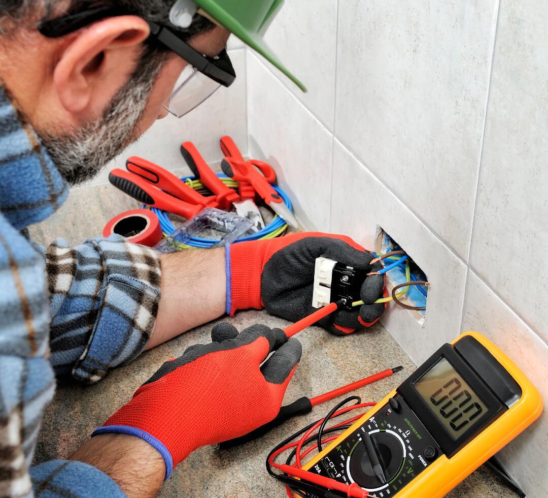 electrician with gloves and safety instruments fixes the electric cable to the socket of a residential installation
