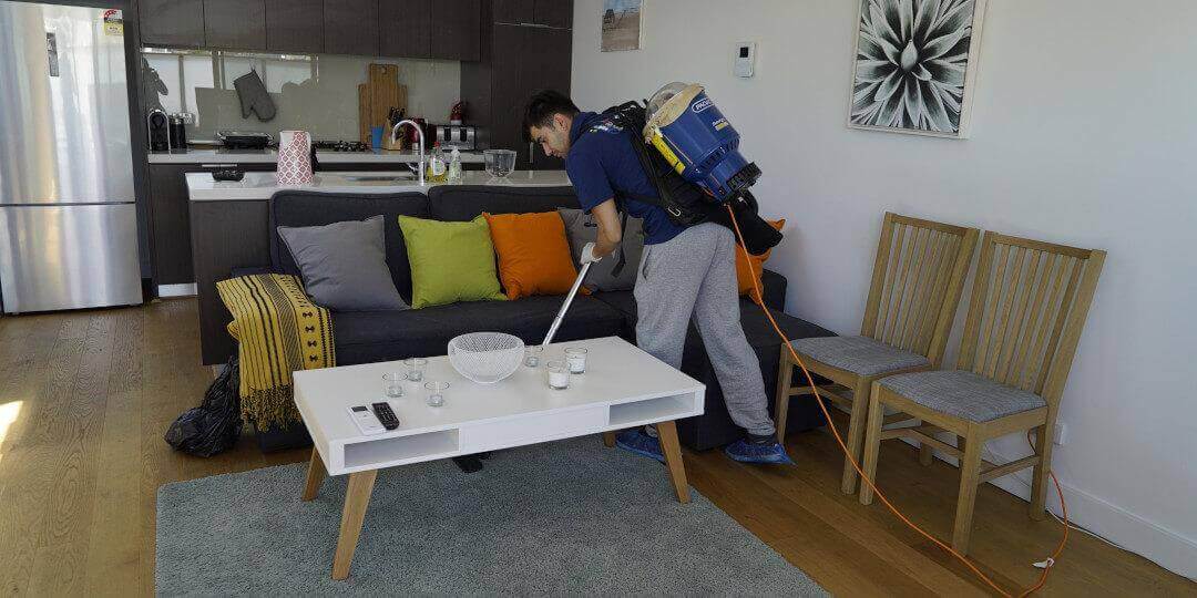 ndis end of lease cleaner vacuuming the floor between a sofa with cushions and a coffee table in the client's living room