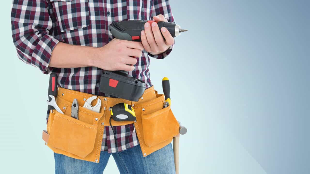 close-up of an NDIS-approved handyman wearing a utility belt and holding a drill in his hands
