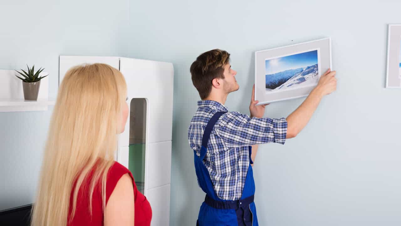 professional handyman fitting a picture on the wall in front of a client